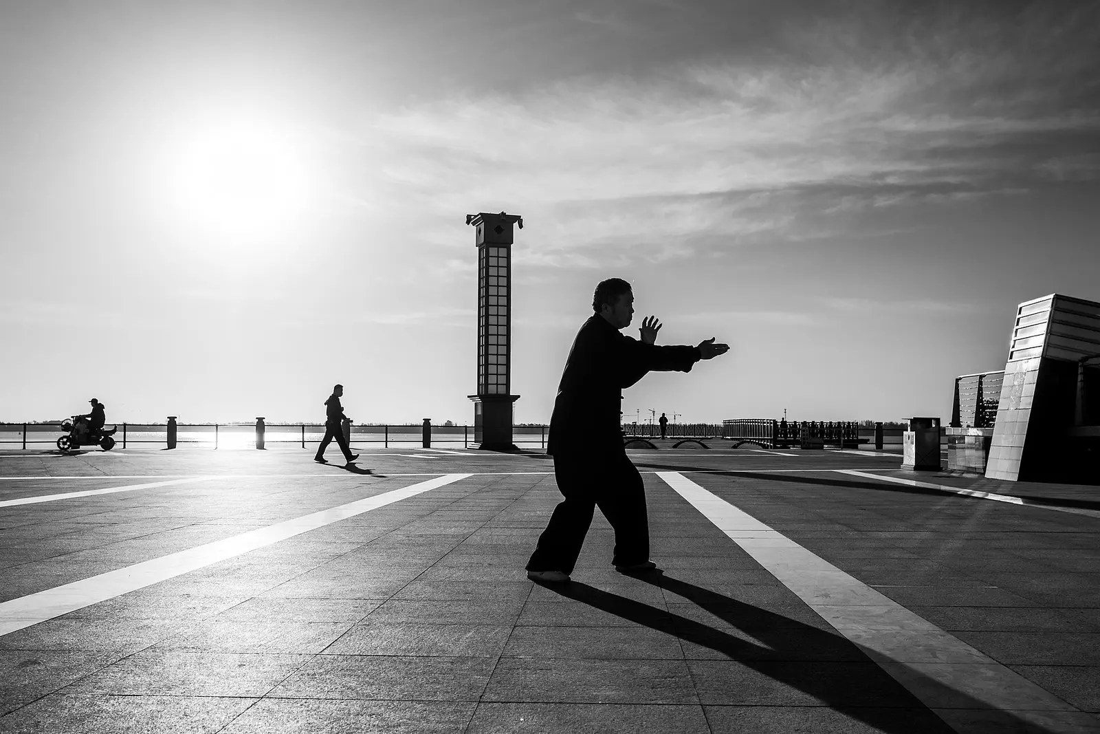 Silhouette of a man practicing a slow Qigong movement on a seaside square at sunrise